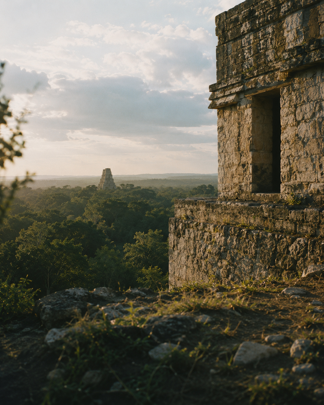 Historic Maya limestone architecture overlooking a forested landscape in late-afternoon light.