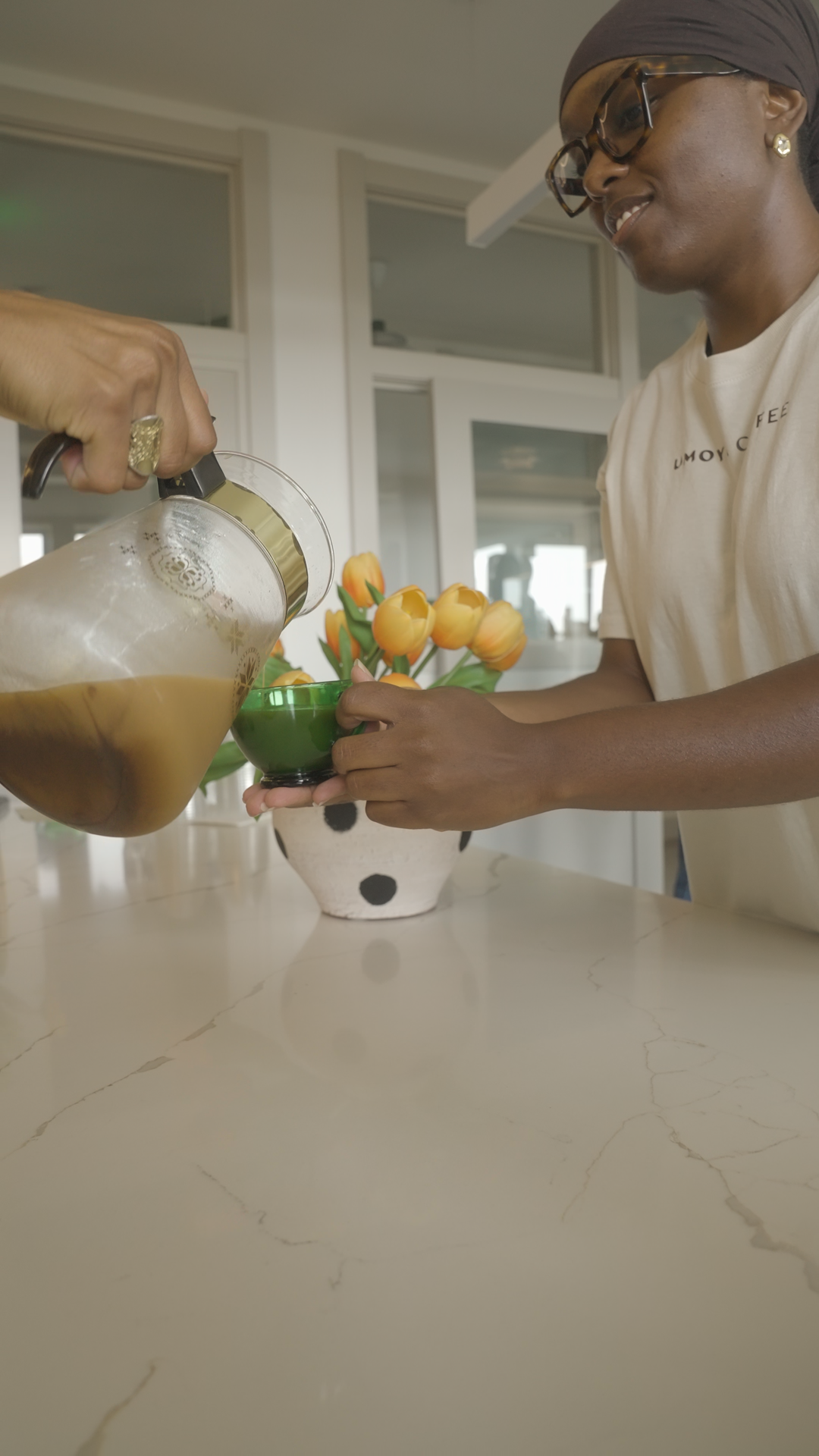 A UMOYA team member in a UMOYA COFFEE shirt pouring coffee into a green cup.